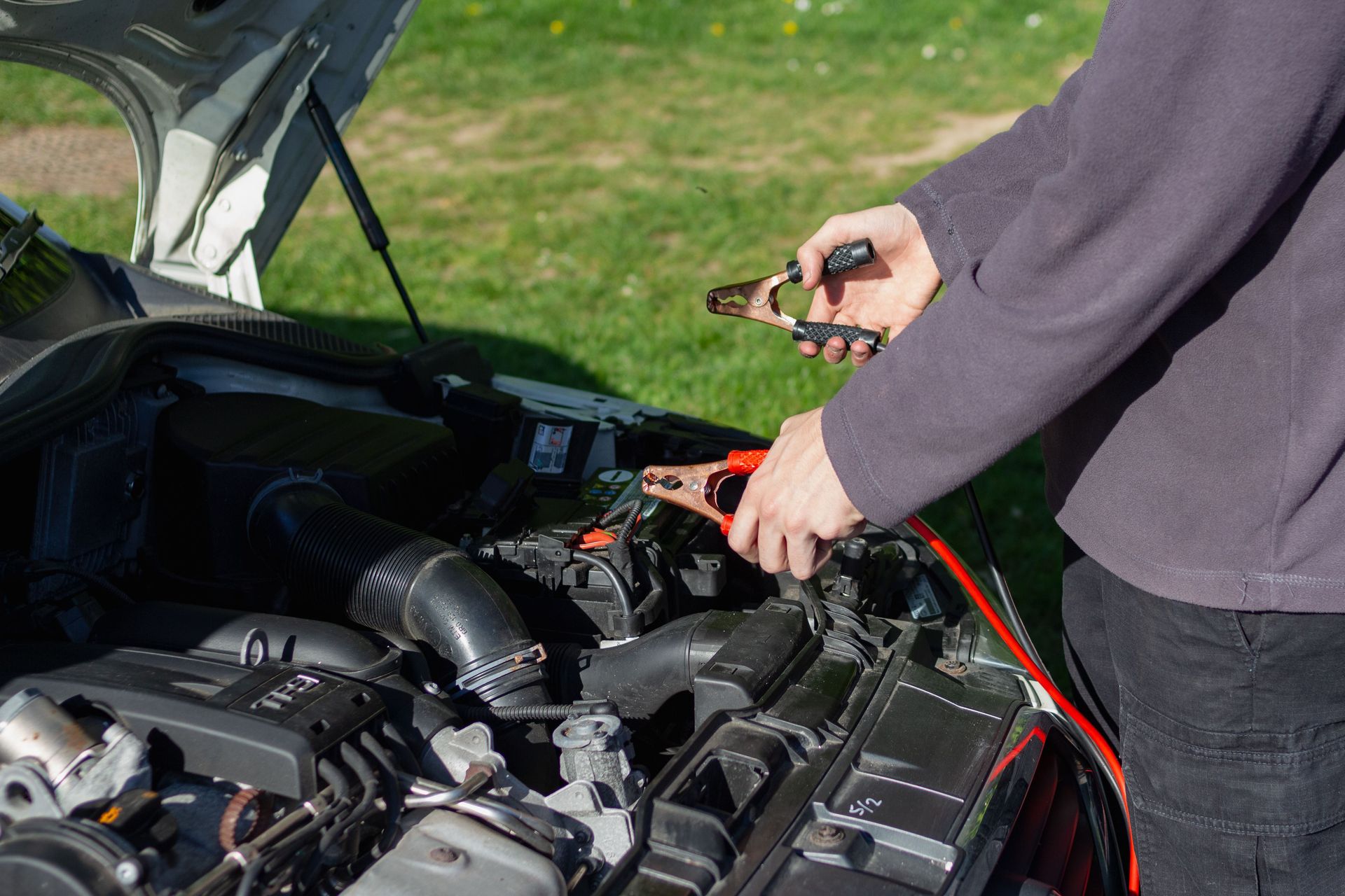 Close-up of mechanic using jumper cables to jump-start a car battery outdoors.