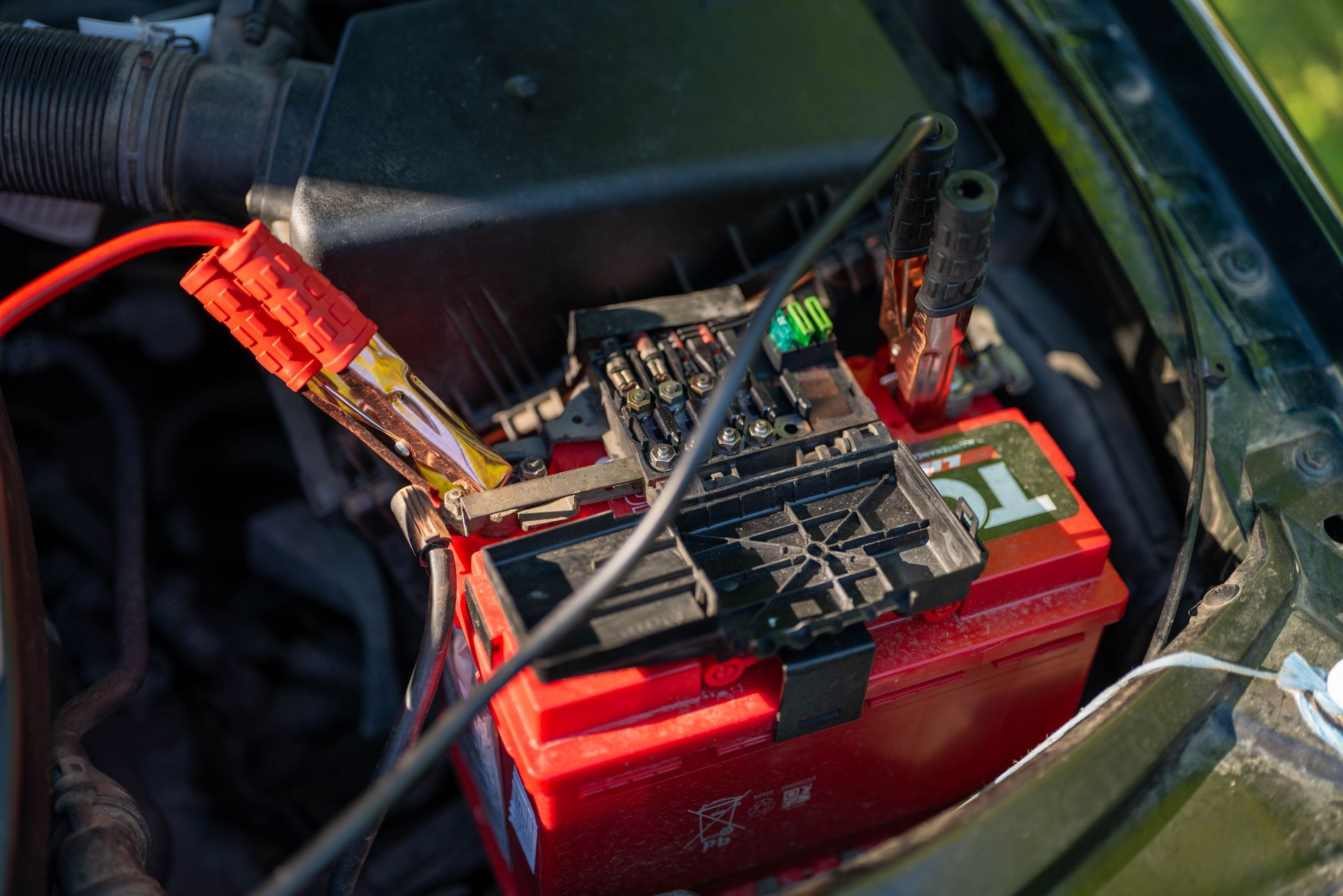 Close-up view of a car battery with red jumper cables connected, outdoors.
